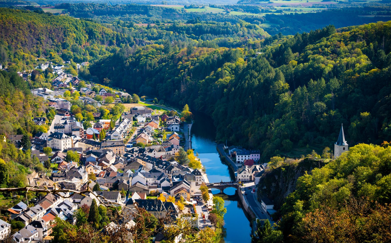 Aerial view of a Luxembourg village in a river bend, autumn forest all around — photograph by Zied Mnif