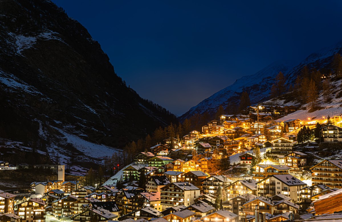 Zermatt village glowing at blue hour beneath dark alpine slopes — photograph by Zied Mnif